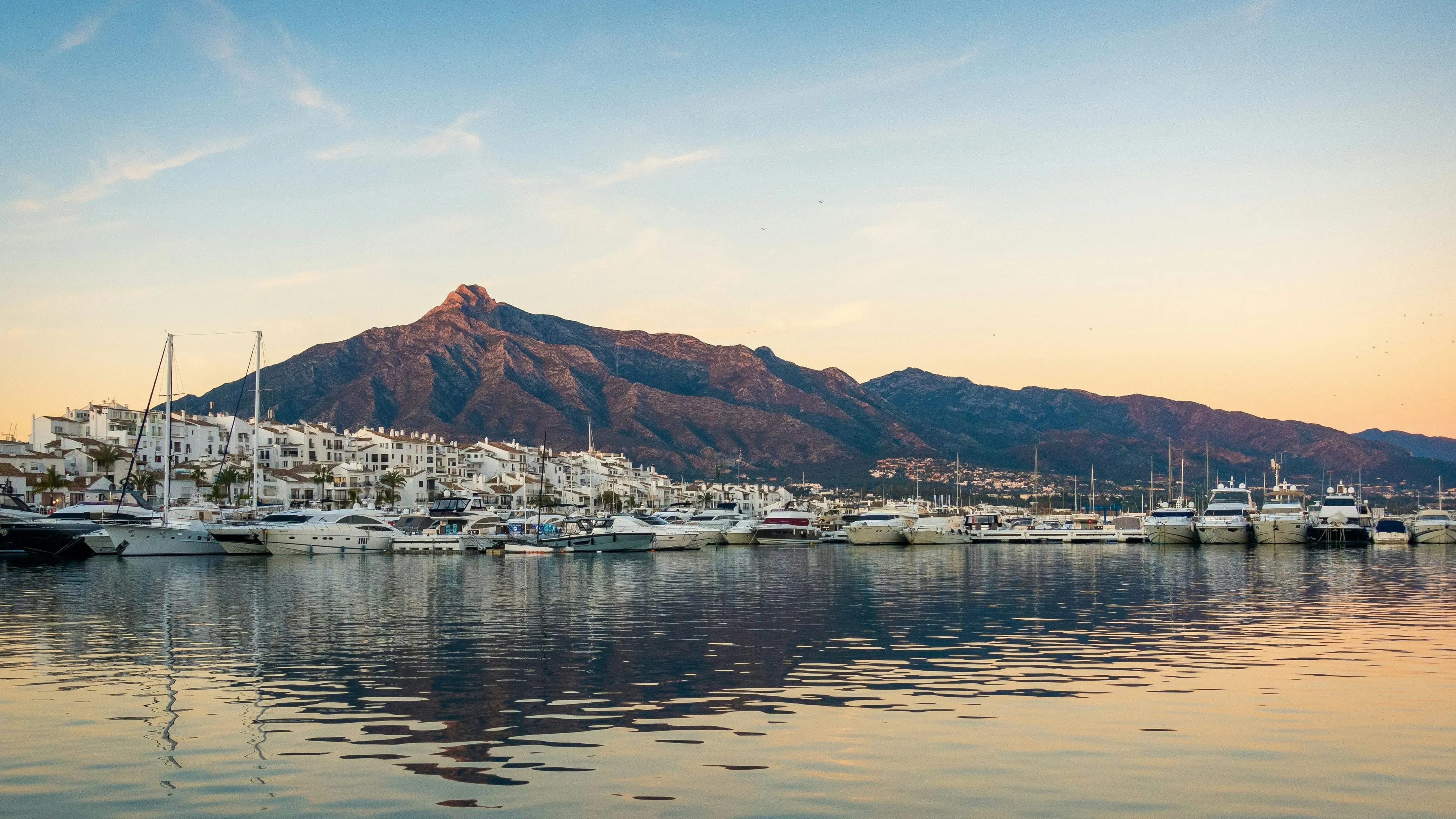 Puerto Banús marina at golden hour, with La Concha rising behind the berths