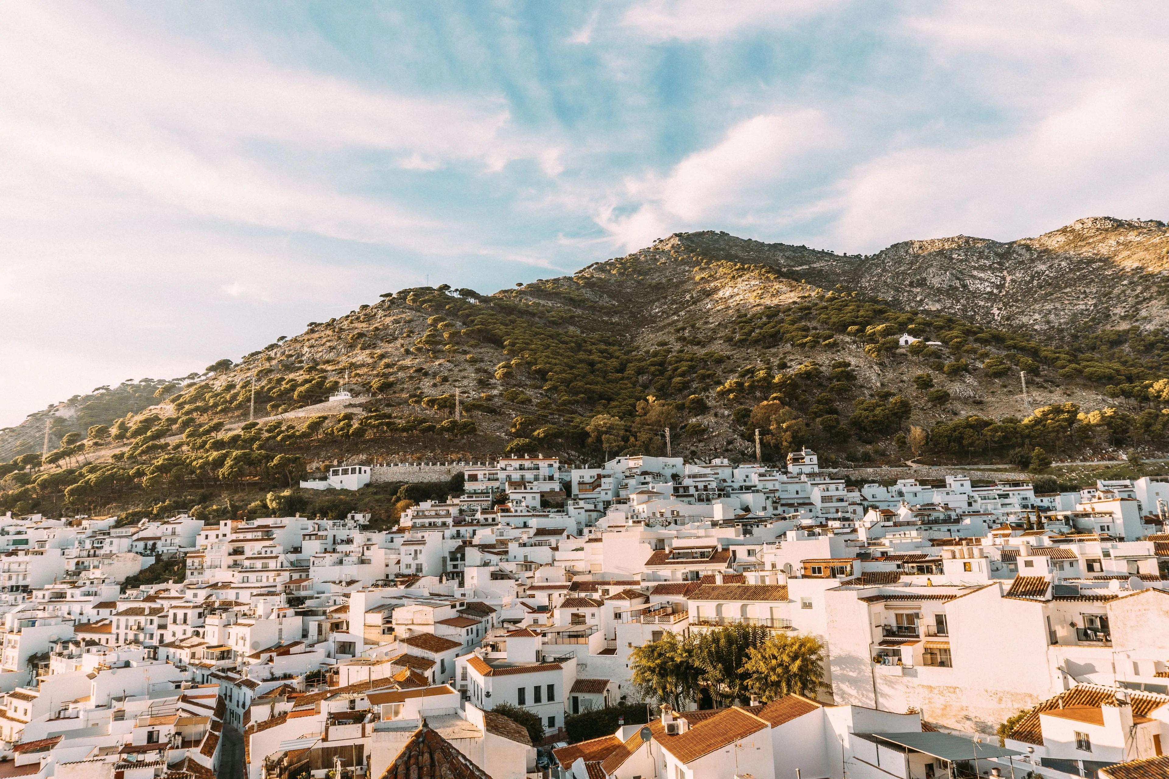 Mijas Pueblo from the air at golden hour, whitewashed houses stepping down the hillside